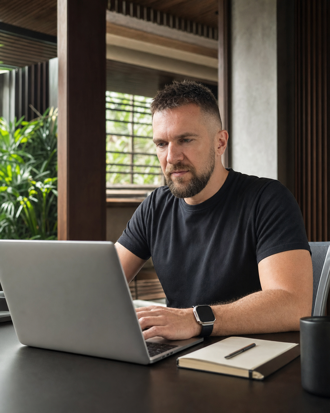 Денис Бугров сосредоточенно работает за MacBook в современном офисе на Бали